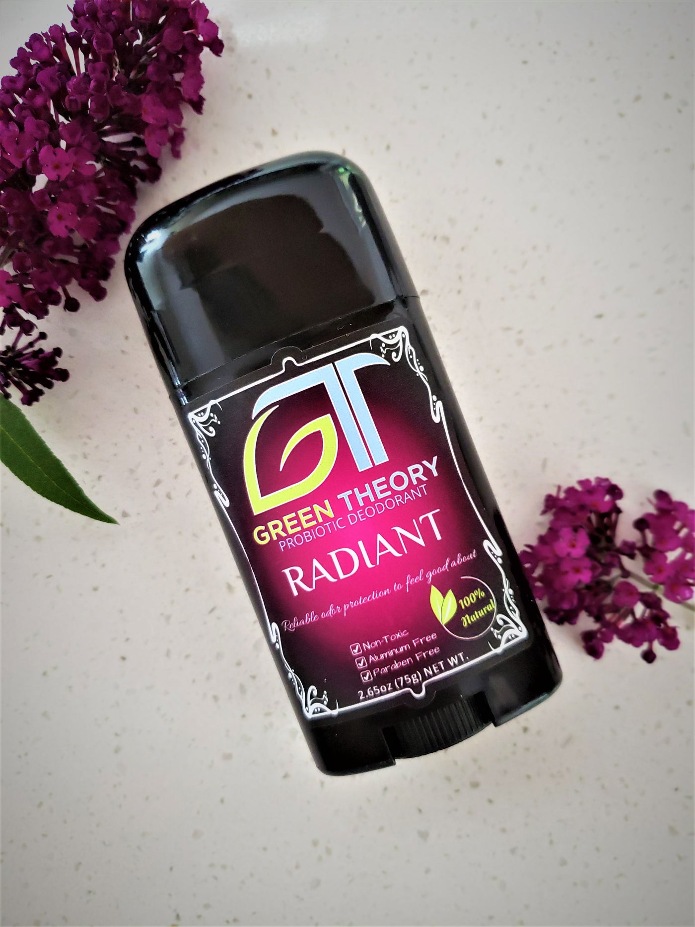 photo of green theory aluminum free probiotic deodorant for women laying on a quartzite counter surrounded by flowers with the same magenta color as the product label