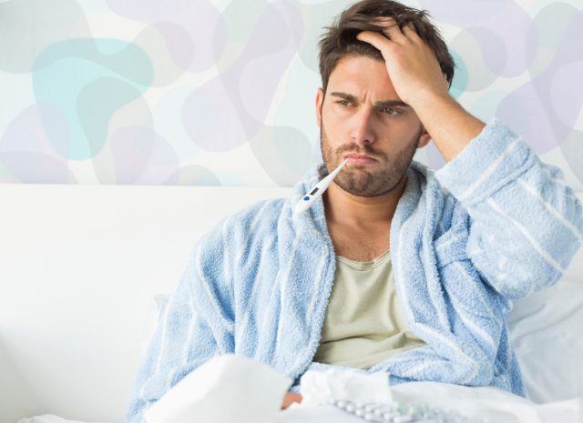 Sick man sitting up in bed with a thermometer in mouth