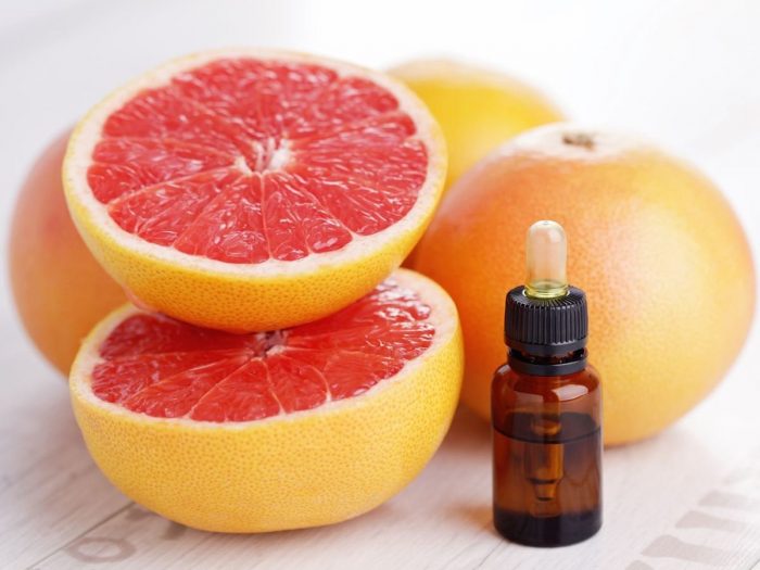 brown bottle of grapefruit essential oil surrounded by cut grapefruit