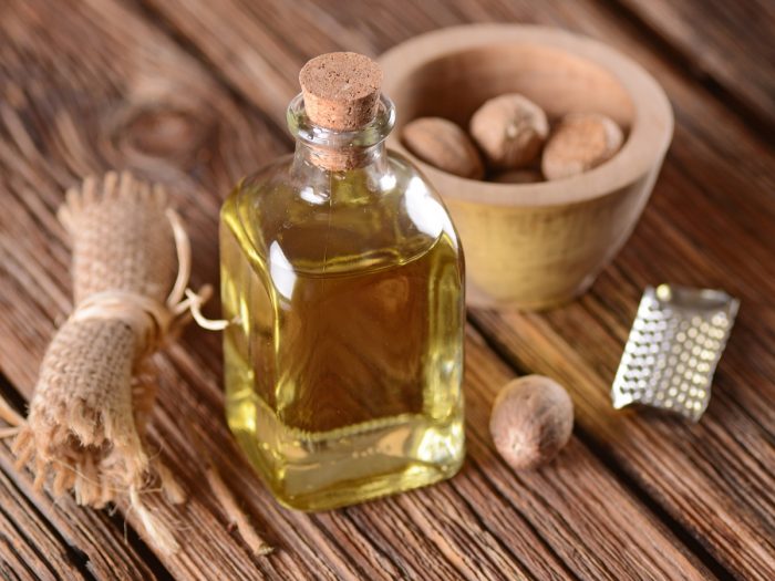 nutmeg essential oil in a clear glass bottle on a wooden table with nuts and grater in the background