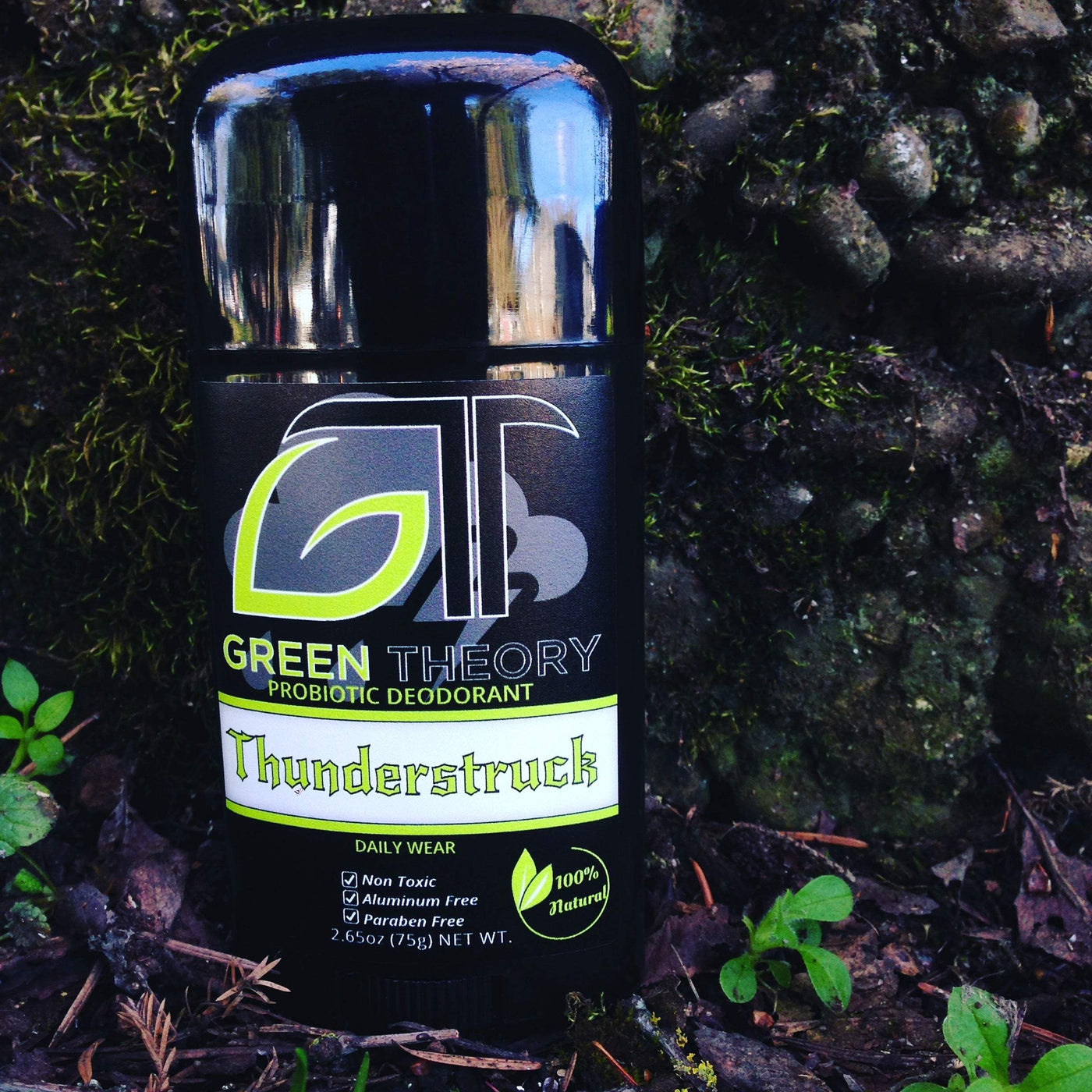 Photo of Green Theory Thunderstruck natural deodorant. Stick is placed against a stone, moss covered wall. Label depicts large Green Theory logo with "thunderstuck" in ACDC looking text