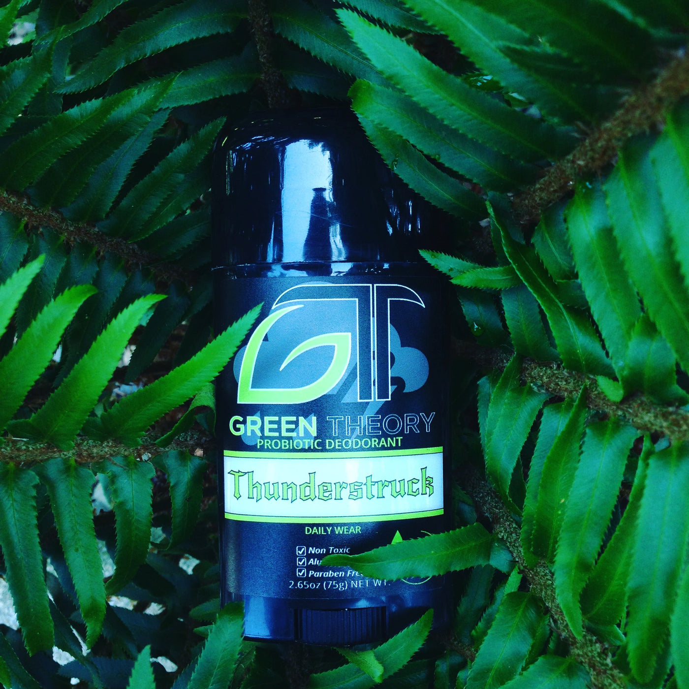 Oversaturated image of Green Theory Thunderstruck probiotic deodorant for men sitting inside the center of a fern plant. 