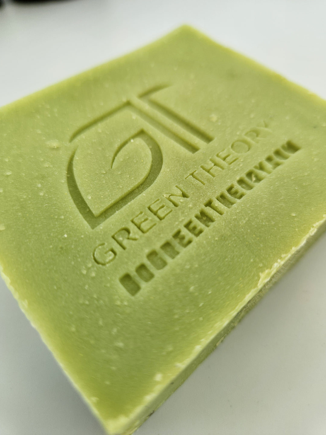 Close up photo of green theory taurus all natural soap. Bar is laying down with its face side up and turned at an angle. soap bar is lime green with the green theory logo and website stamped into the bar