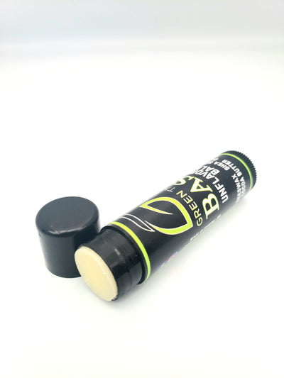 angular photo of green theory basic unflavored lip balm laying with the cap off to show texture against a white background