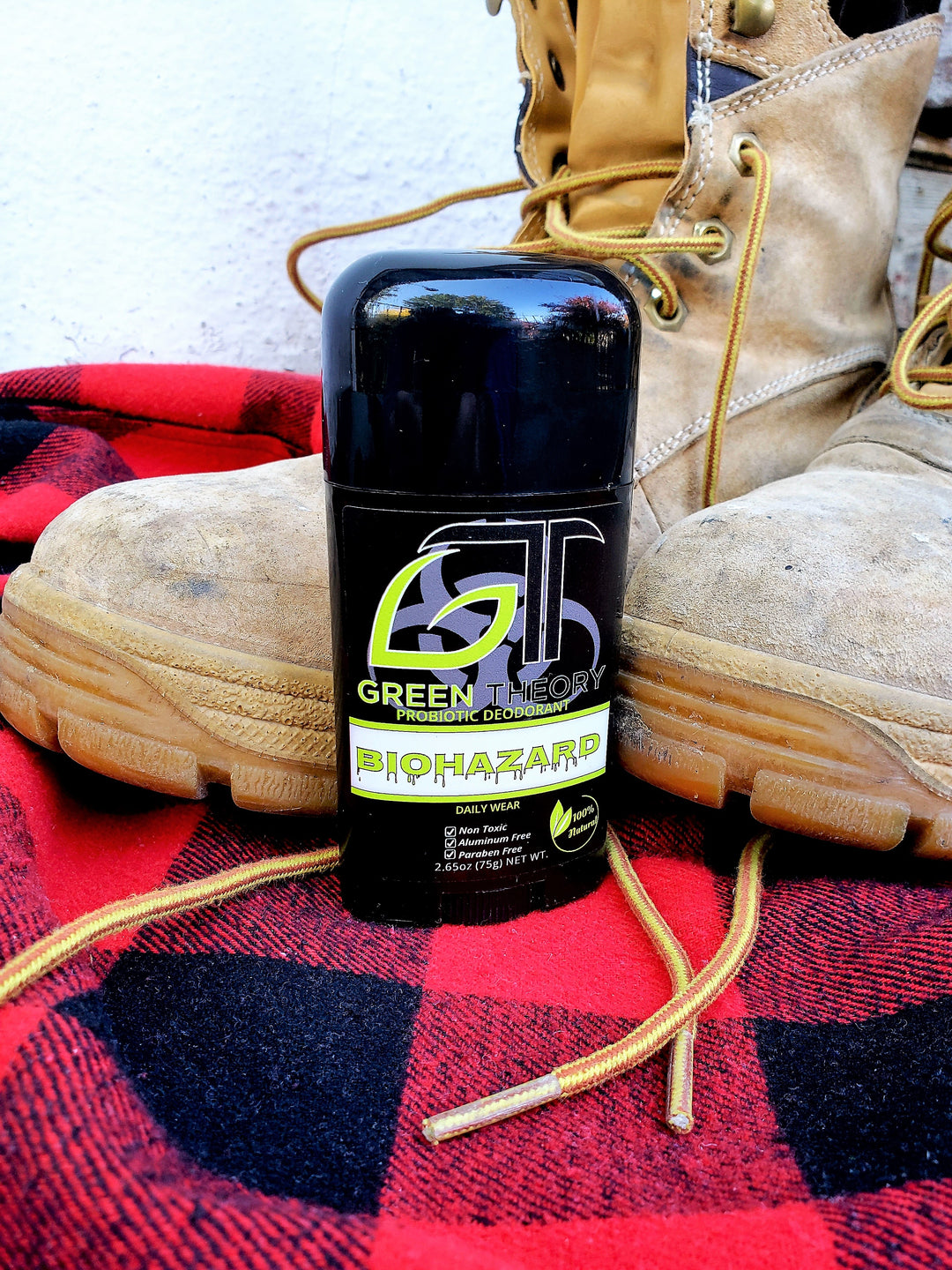 Stick of green theory biohazard probiotic natural deodorant standing on a red flannel fabric with work boots in the background