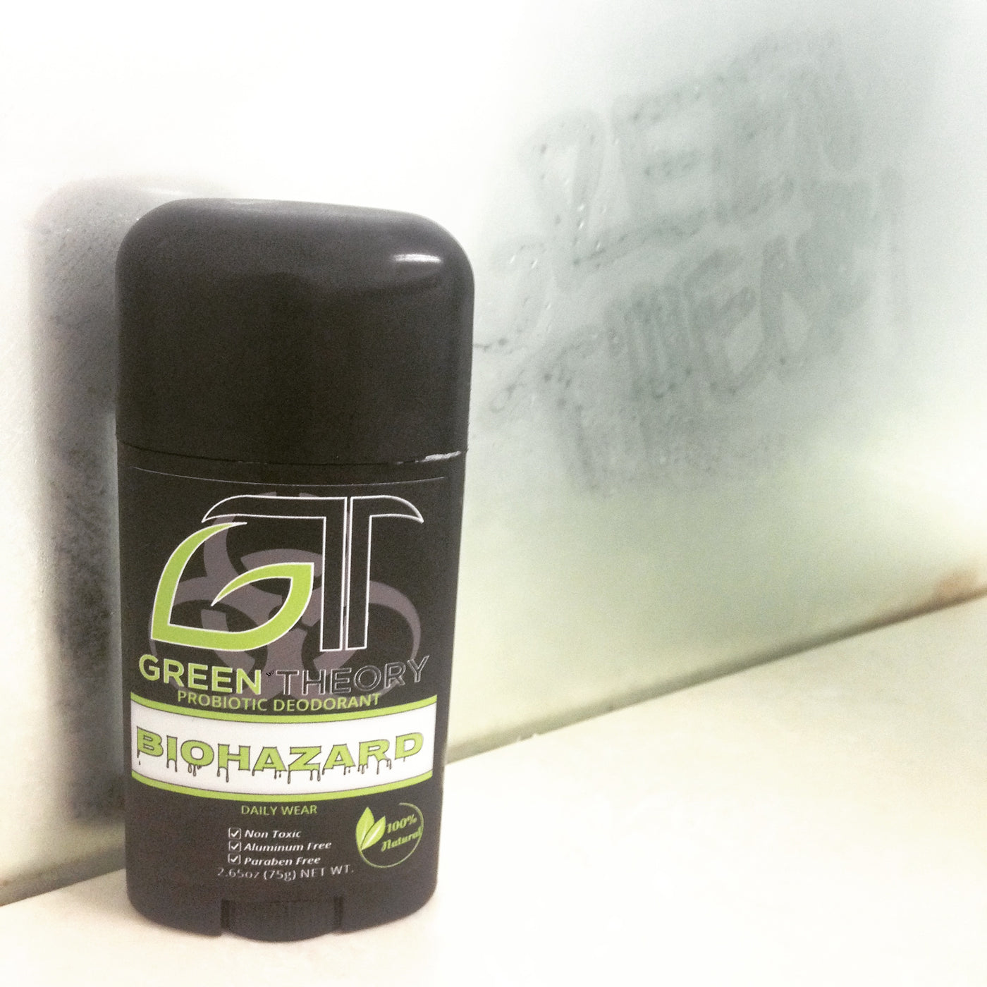 Photo of green theory biohazard probiotic natural deodorant on a bathroom shelf a steamy mirror behind it. The mirror has "green theory" written in it. 