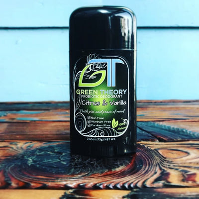 photo of green theory citrus and vanilla aluminum free deodorant sitting on a burnt wood table with baby blue background