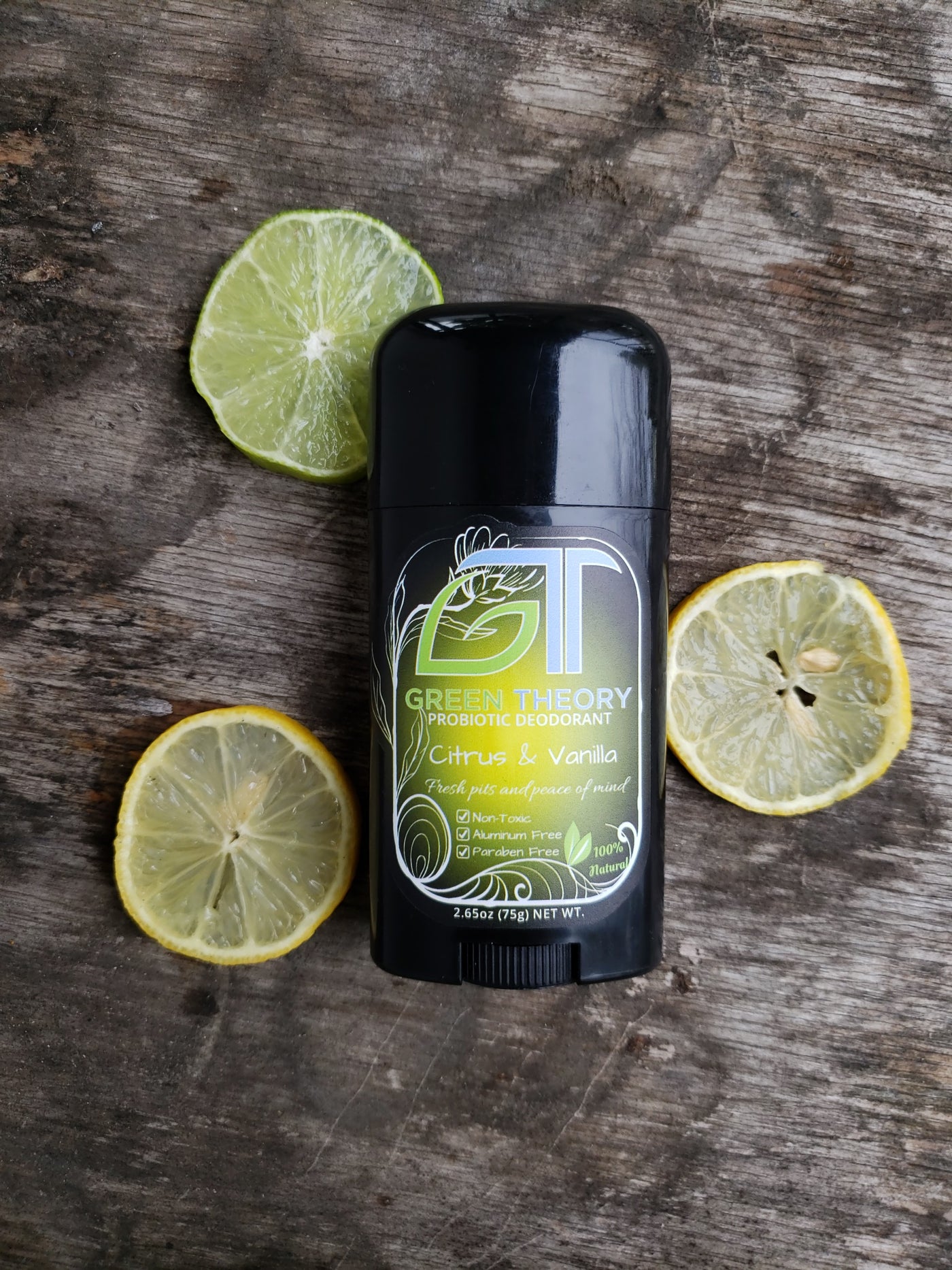 photo of green theory citrus and vanilla probiotic natural deodorant laying on a wood grain background with slices of lemon and lime around it