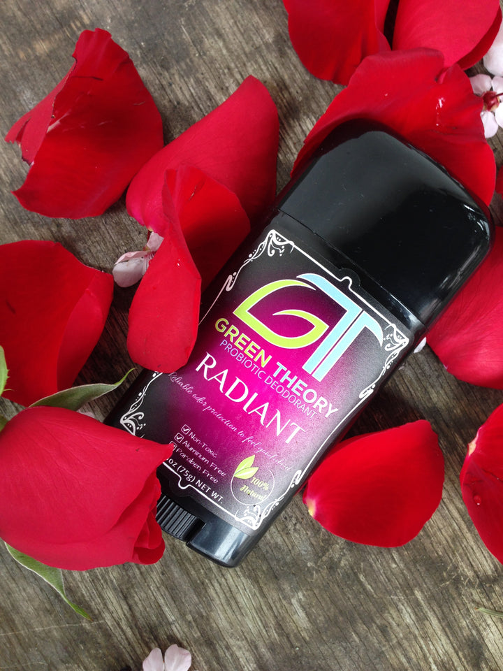 photo of green theory radiant probiotic natural aluminum free deodorant laying on a wood grain texture surrounded by rose petals