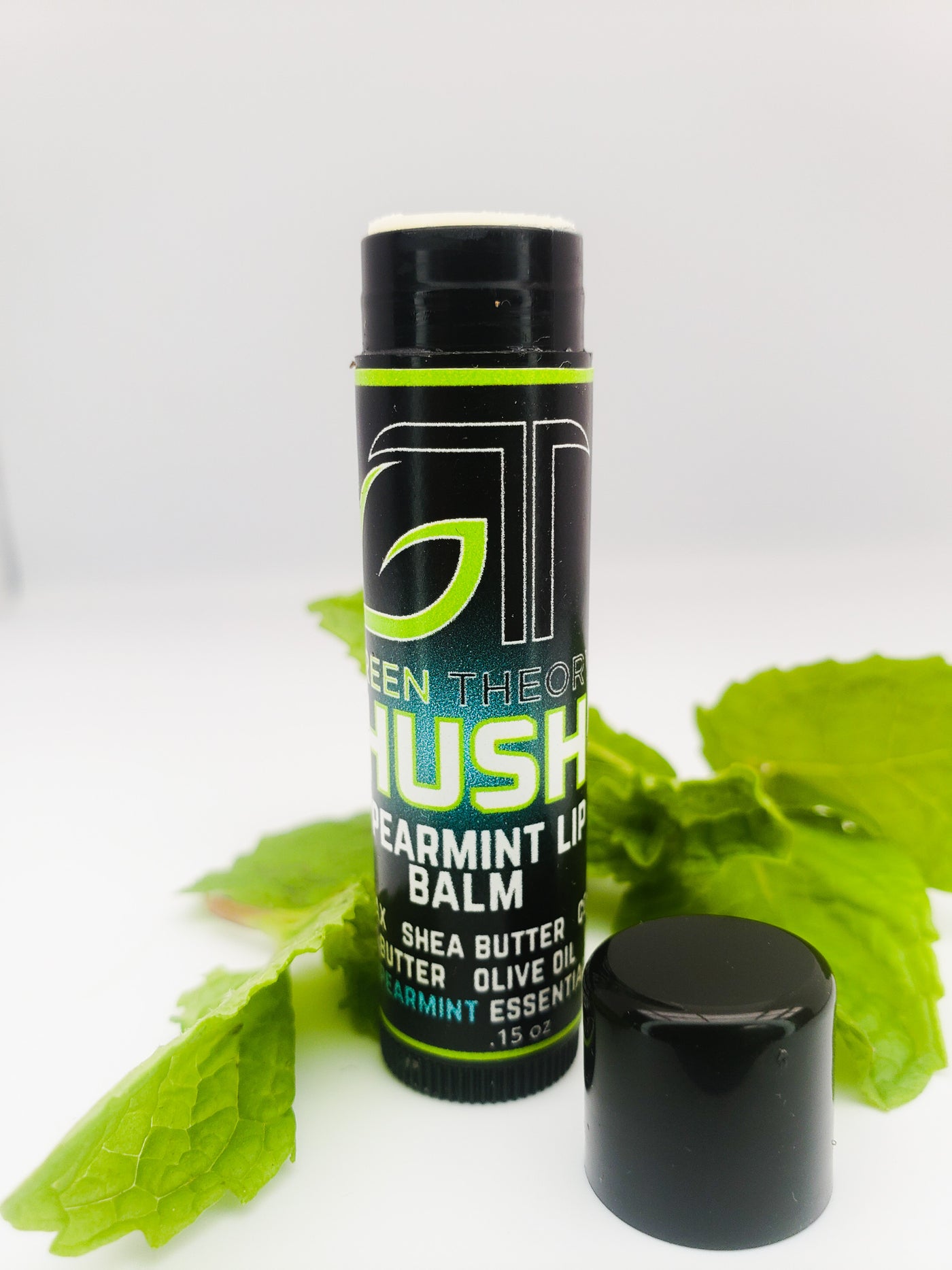 photo of Green Theory Hush all natural lip balm standing with cap taken off and sitting beside the stick of lip balm. Background is all white with a spearmint leaf laying behind the lip balm